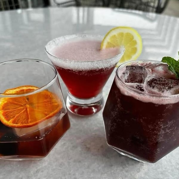 Three vibrant cocktails on a white table: an Old Fashioned, a pink martini, and a dark berry drink.