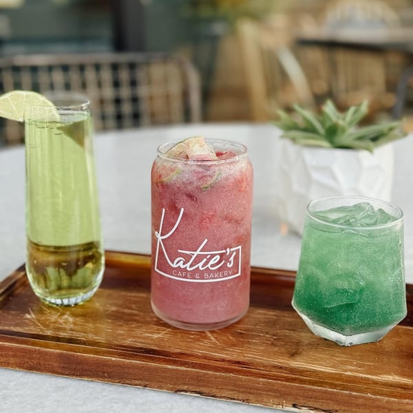 Three colorful drinks, green, red, and blue, on a wooden tray with a succulent plant.