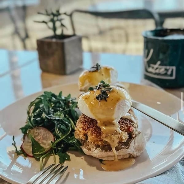 Eggs Benedict with hollandaise sauce, crab cake, and a side salad on a white plate.