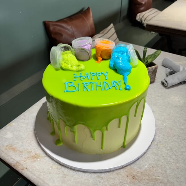A vibrant green birthday cake with colorful slime spilling from small containers on top.