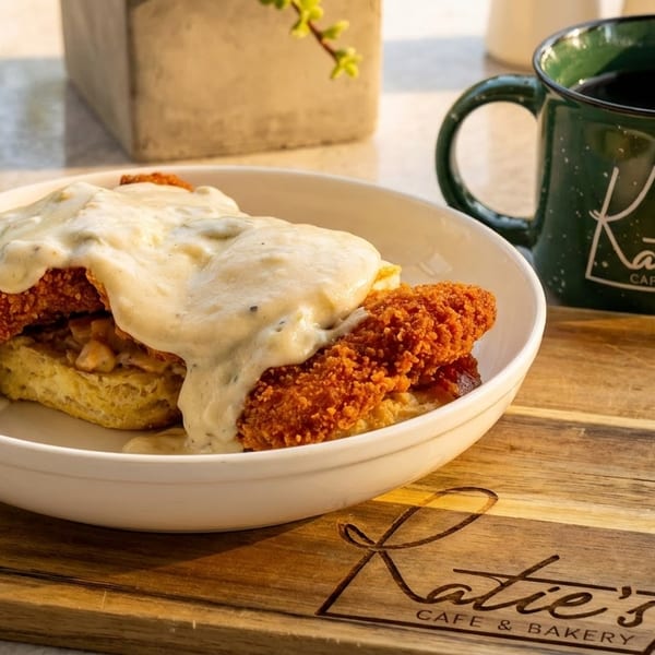 Fried chicken and biscuits with gravy in a white bowl, next to a Katie's Cafe & Bakery mug.