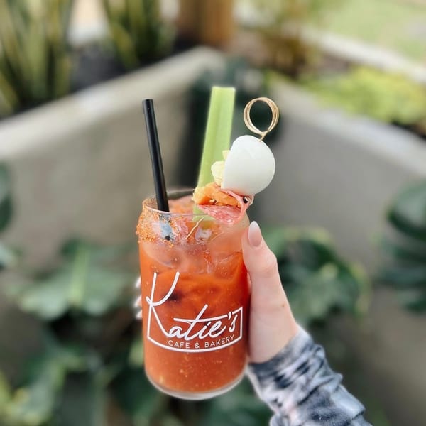 Hand holding a Katie's Cafe & Bakery Bloody Mary garnished with celery, salami, and mozzarella.