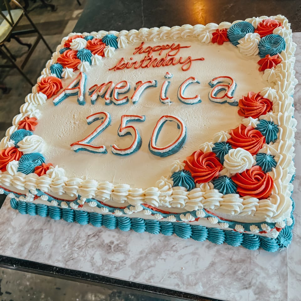 Square white cake with red, white, and blue frosting, reading "Happy Birthday America 250".